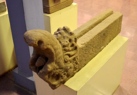 Makara-headed water-chute: Sandstone, 7th century: The makara is a mythical aquatic animal that resembles a crocodile with a trunk. Because of its aquatic association, it is often used, as here, in architectural details concerning the channeling of water, such as spouts, or for directing springs. This makara piped water that filtered through the sacred mountain that towers over Wat Phu. The water, which was already blessed by the linga at the summit, passed through the sanctuary, and over the altar, pouring a steady trickle of holy water for pilgrims to the temple to lustrate themselves with.