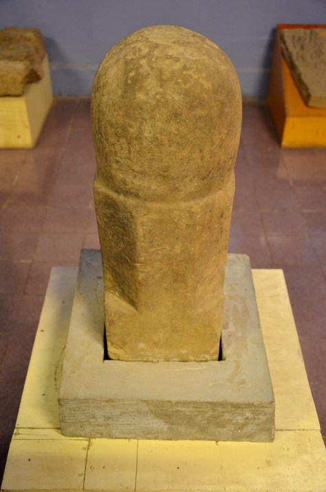 Linga: Sandstone, c 11th century: The linga represents the Hindu god Shiva, in the form of a stylized phallus, and is one of the most important and potent symbols of Hinduism. This particular style of linga actually represents the trimurti, the holy trinity of the Hindu gods. The square base stands for Brahma, creator of the Universe, the octagonal section for Vishnu, and the top, rounded section is for Shiva. The site of Wat Phu, from which it originated, was chosen for its proximity to Lingaparvata, a mountain in the southern Lao province of Champasak, auspicious due to the linga-like stone outcrop that caps it.