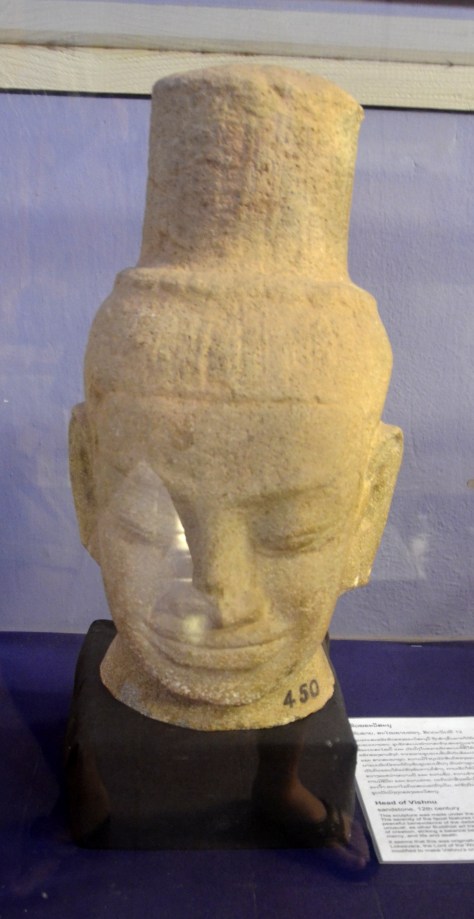 Head of Vishnu: Sandstone, 12th century: This sculpture was made under the influence of Angkor's Bayon style. The serenity of the facial features is typical of art of this period. The peaceful benevolence of the deities the Angkorian style depicts is unusual, as other Buddhist art traditions tend to represent all aspects of creation, striking a balance between good and evil, wrath and mercy, and life and death. It seems that this was originally a sculpture of the Buddhist deity Lokesvara, the Lord of the World, but his elaborate hairstyle has been modified to make Vishnu's crown.